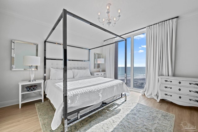 bedroom featuring a wall of windows, a chandelier, light hardwood / wood-style flooring, and a water view