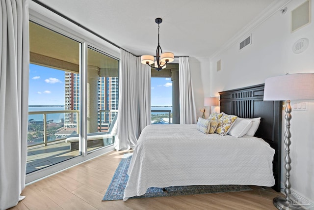 bedroom with access to outside, a water view, light wood-type flooring, ornamental molding, and a chandelier