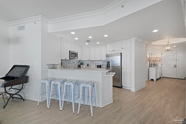 kitchen featuring a breakfast bar area, stainless steel appliances, kitchen peninsula, white cabinets, and tasteful backsplash