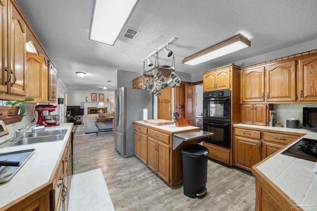 kitchen featuring black appliances, light wood finished floors, and brown cabinets