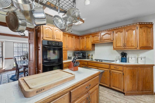 kitchen featuring brown cabinets, light countertops, decorative backsplash, a textured ceiling, and black appliances