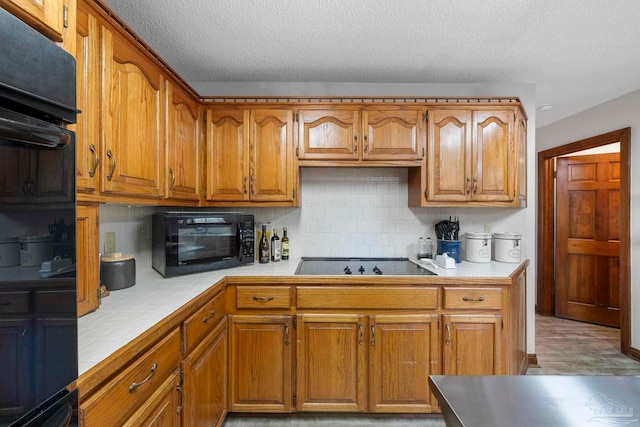 kitchen with light countertops, backsplash, brown cabinetry, a textured ceiling, and black appliances