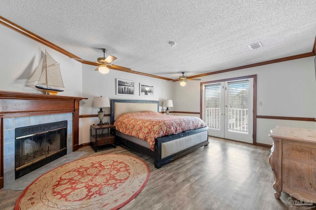 bedroom featuring visible vents, a tile fireplace, wood finished floors, access to outside, and crown molding