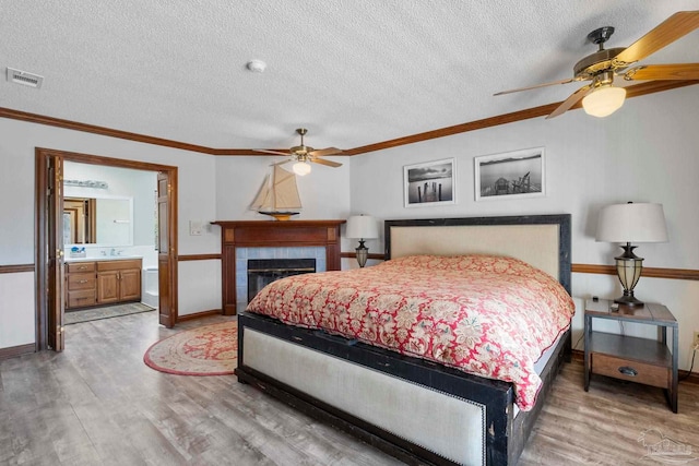 bedroom featuring a textured ceiling, a fireplace, wood finished floors, visible vents, and ornamental molding