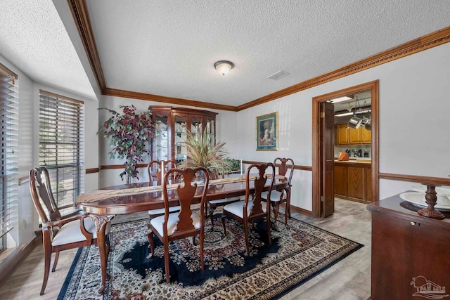 dining area with a textured ceiling, visible vents, and crown molding