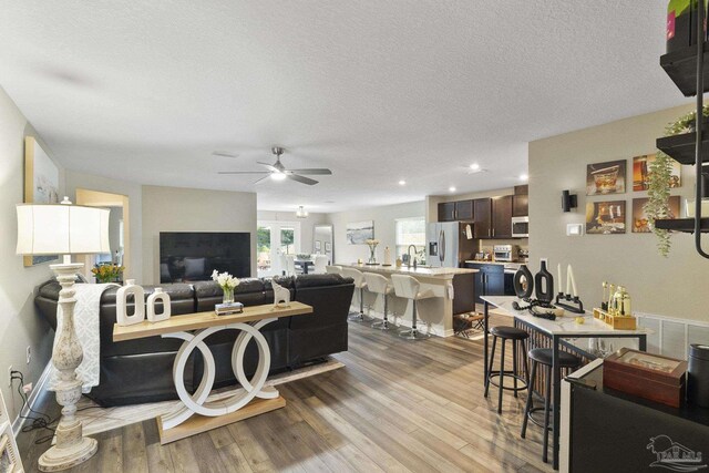 living room with a textured ceiling, light wood-style flooring, and a ceiling fan