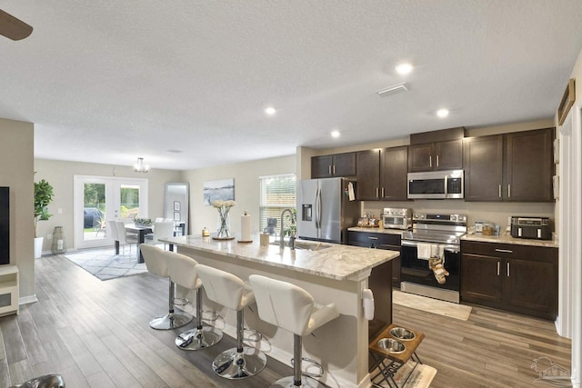 kitchen with a breakfast bar area, stainless steel appliances, a sink, light wood-type flooring, and an island with sink