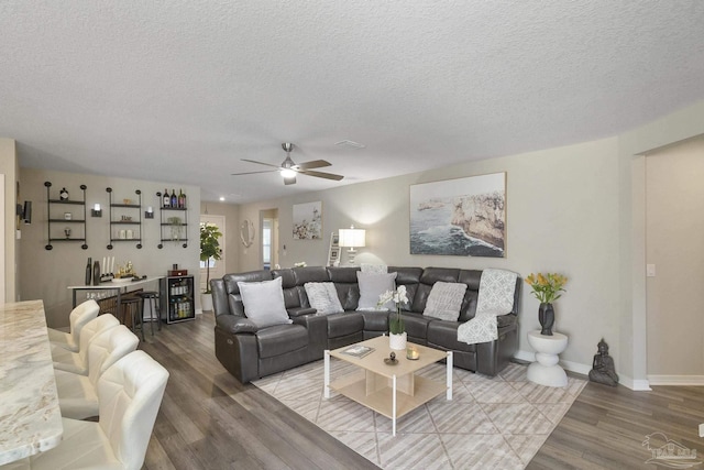 living room featuring baseboards, ceiling fan, wood finished floors, a textured ceiling, and a bar