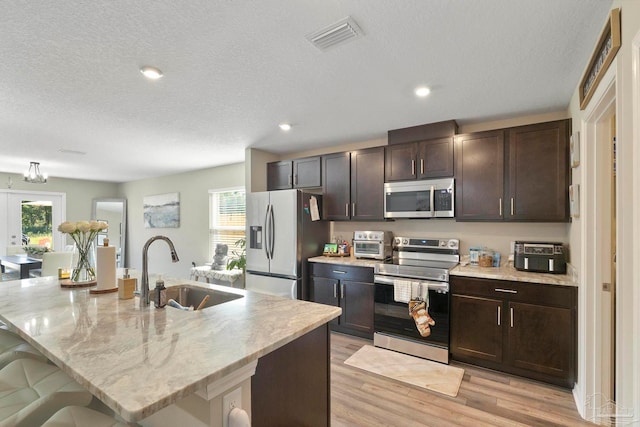 kitchen with sink, light hardwood / wood-style flooring, an island with sink, a breakfast bar area, and stainless steel appliances