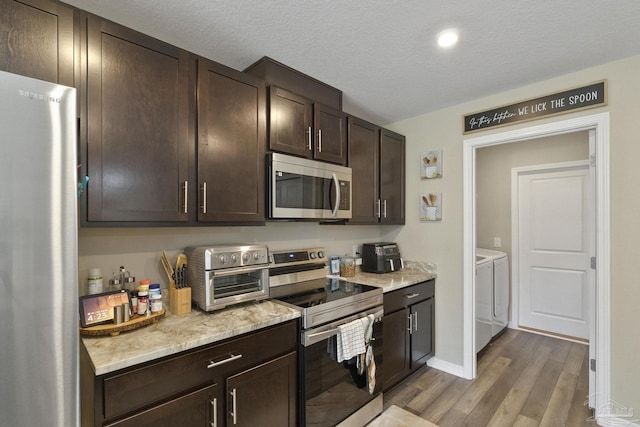 kitchen featuring stainless steel appliances, washer and dryer, dark brown cabinets, and wood finished floors