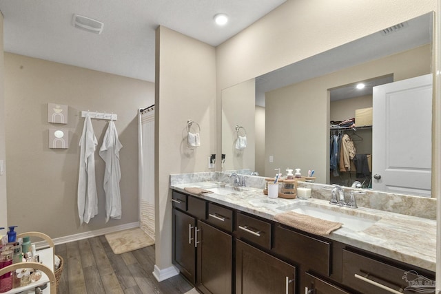 full bath featuring double vanity, wood finished floors, a sink, and a walk in closet