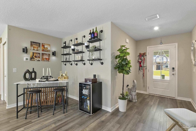 bar with a dry bar, beverage cooler, visible vents, wood finished floors, and a textured ceiling