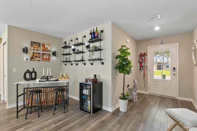 bar with a textured ceiling, wine cooler, and wood-type flooring