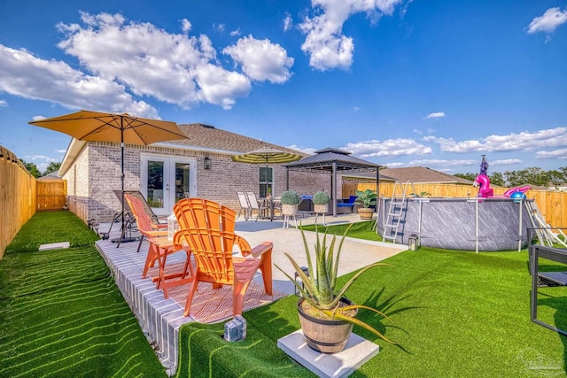 rear view of house with a fenced in pool, a lawn, a gazebo, french doors, and brick siding