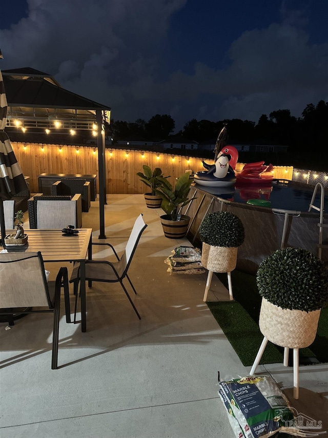 patio at twilight featuring outdoor dining space, a fenced backyard, and a gazebo