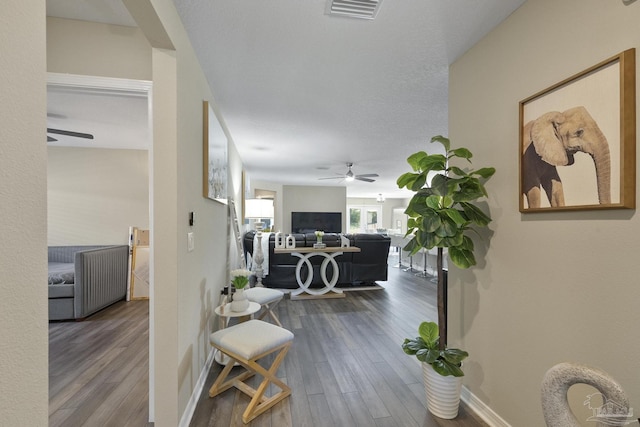 hall featuring baseboards, a textured ceiling, visible vents, and wood finished floors