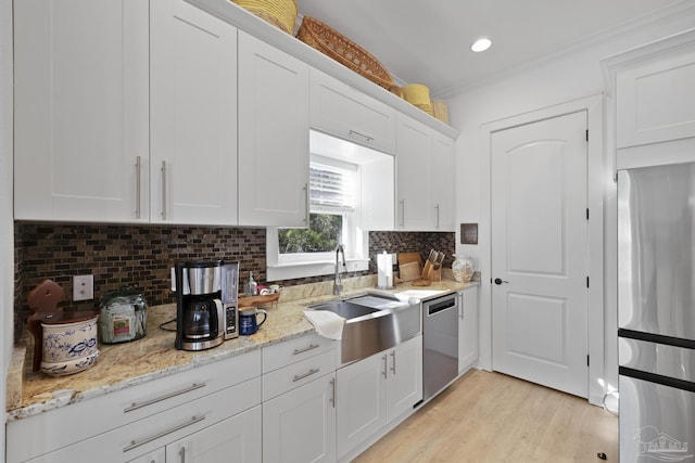 kitchen featuring stainless steel appliances, decorative backsplash, white cabinets, a sink, and light wood-type flooring