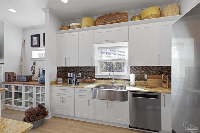 kitchen featuring white cabinets, appliances with stainless steel finishes, light stone countertops, crown molding, and a sink