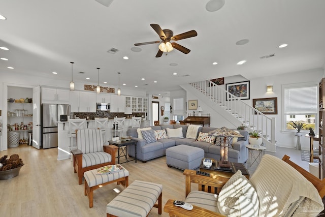 living area featuring stairs, light wood-type flooring, visible vents, and a ceiling fan