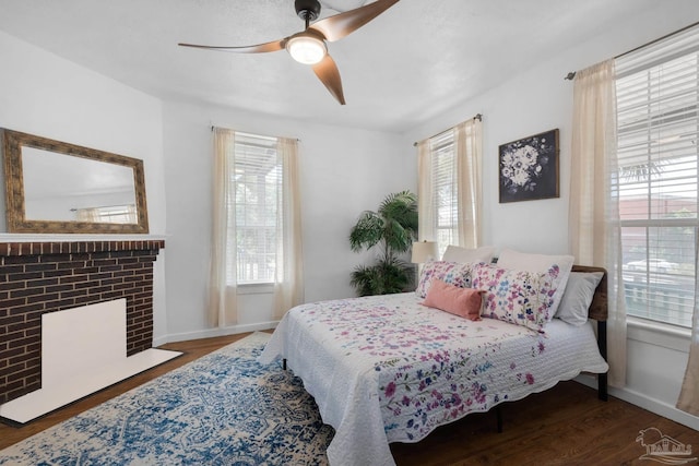 bedroom with dark hardwood / wood-style flooring, ceiling fan, and a brick fireplace