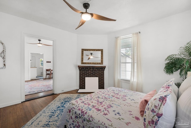 bedroom featuring dark hardwood / wood-style flooring, ceiling fan, and a brick fireplace