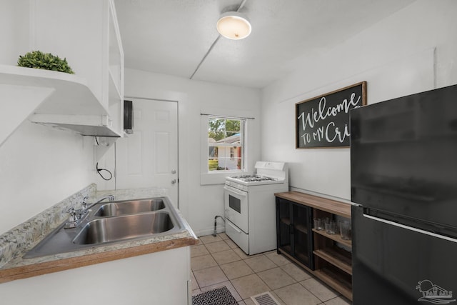 kitchen featuring light tile patterned floors, black fridge, white range with gas cooktop, and sink