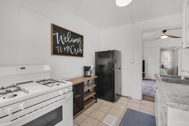 kitchen featuring sink, black refrigerator, light tile patterned floors, white range with gas stovetop, and ceiling fan