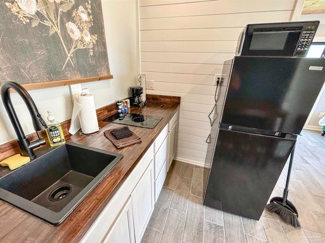 kitchen featuring black appliances, light hardwood / wood-style flooring, sink, and wood counters