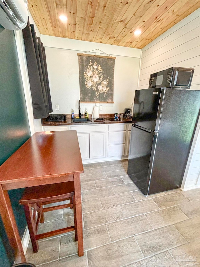 kitchen with stainless steel fridge, white cabinets, wood walls, wooden ceiling, and sink