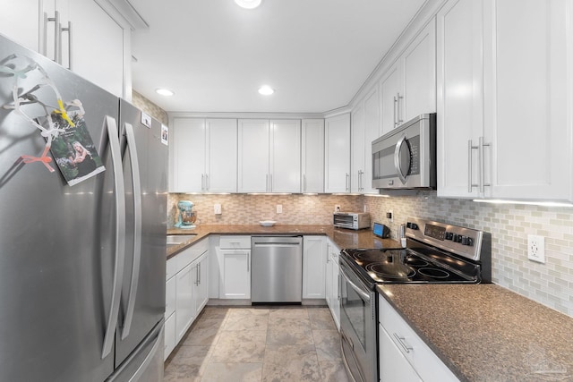 kitchen with white cabinets, decorative backsplash, appliances with stainless steel finishes, and dark stone countertops