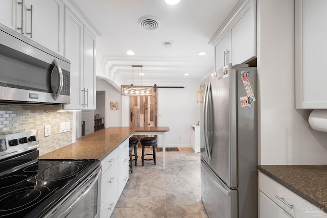 kitchen with stainless steel appliances, a barn door, white cabinetry, and dark stone counters