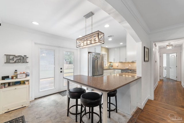 kitchen featuring white cabinetry, stainless steel refrigerator, a kitchen breakfast bar, kitchen peninsula, and light hardwood / wood-style flooring