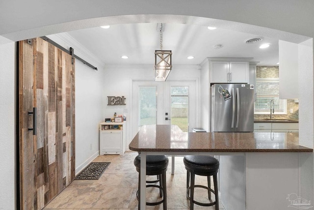 kitchen with white cabinetry, a barn door, a kitchen bar, stainless steel refrigerator, and sink