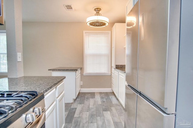 kitchen featuring dark stone counters, stainless steel refrigerator, light wood-type flooring, and white cabinets