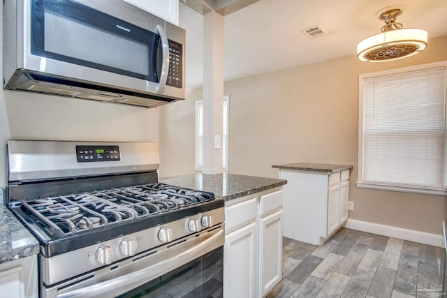 kitchen with dark stone countertops, white cabinetry, light hardwood / wood-style flooring, and stainless steel appliances