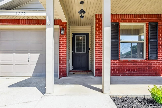 property entrance with a garage, brick siding, concrete driveway, and covered porch