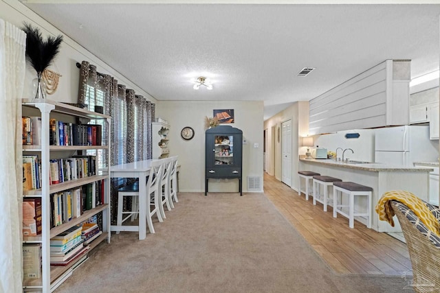 interior space with light carpet, visible vents, light wood finished floors, and a textured ceiling