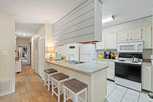 kitchen with visible vents, a sink, a kitchen breakfast bar, white appliances, and a peninsula