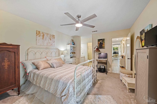 bedroom featuring a ceiling fan, light colored carpet, visible vents, and a textured ceiling