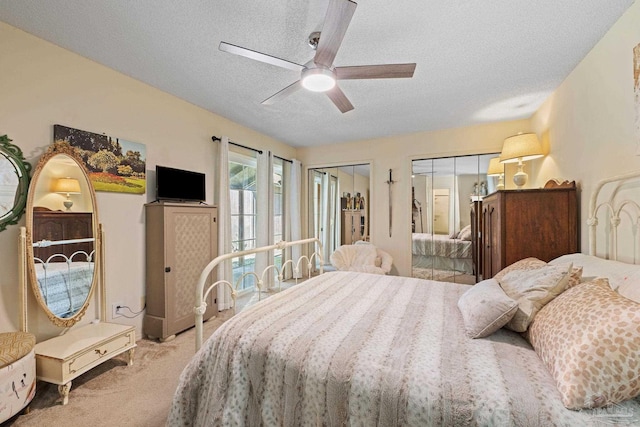 bedroom featuring multiple closets, a textured ceiling, light carpet, and a ceiling fan