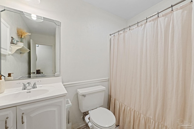 full bathroom with vanity, toilet, wainscoting, and a decorative wall