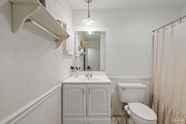 full bath featuring a wainscoted wall, toilet, vanity, and a textured wall