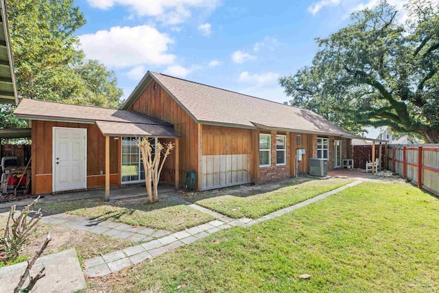 rear view of house with a patio, central AC unit, fence, a yard, and a shingled roof