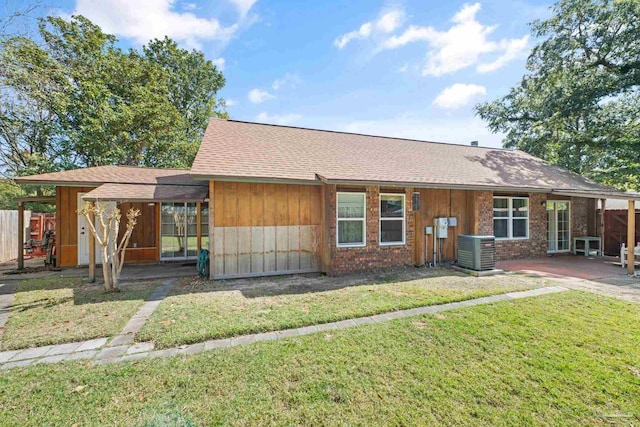 view of front of house with a front lawn, cooling unit, roof with shingles, and a patio