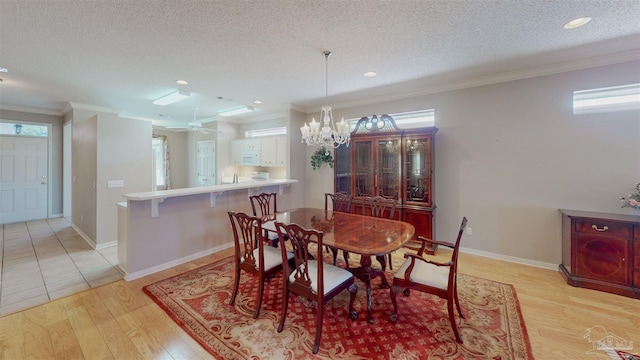 dining room featuring a notable chandelier, ornamental molding, a textured ceiling, and light wood-type flooring