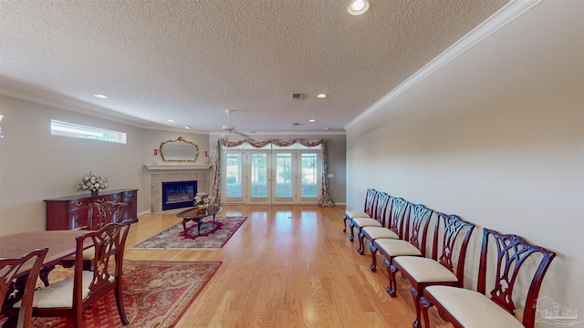 living room featuring a tile fireplace, ornamental molding, ceiling fan, and light wood-type flooring