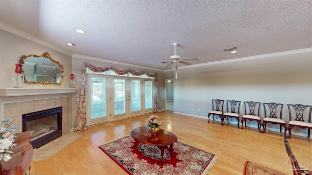 living room featuring hardwood / wood-style flooring, a tiled fireplace, ceiling fan, crown molding, and a textured ceiling