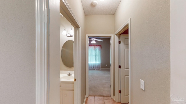 corridor featuring light colored carpet, sink, and a textured ceiling