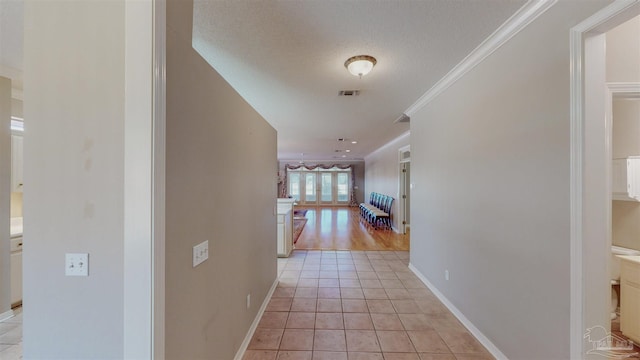 hall featuring light tile patterned flooring, ornamental molding, and a textured ceiling