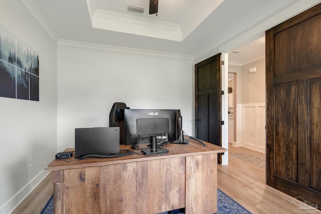 office space with visible vents, a raised ceiling, light wood finished floors, and crown molding